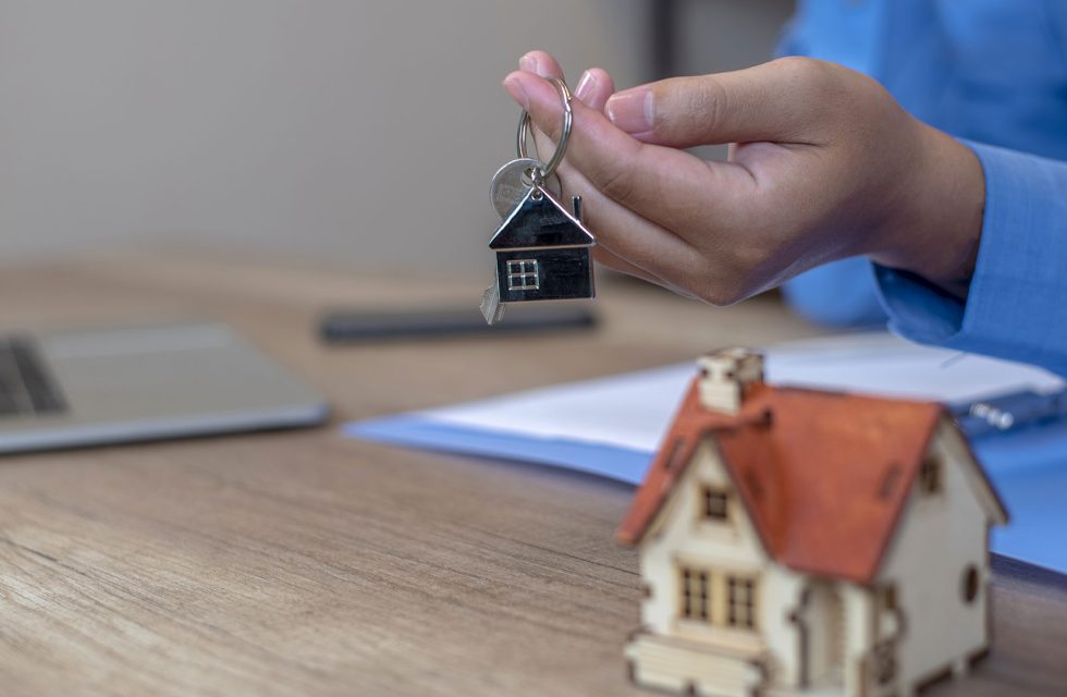 Hand holding home keychain and house model. Property investment and house mortgage financial real estate